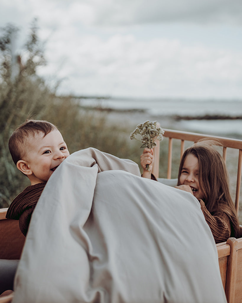 Smilende dreng og pige i barneseng omfavnet af økologisk sengetøj fra Favn København